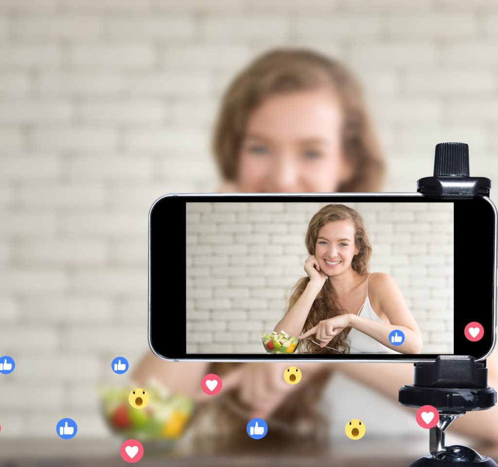 Young female blogger and vlogger and online influencer live streaming a cooking show on social media using a smartphone